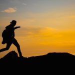A silhouette of a person running on a hill at sunset