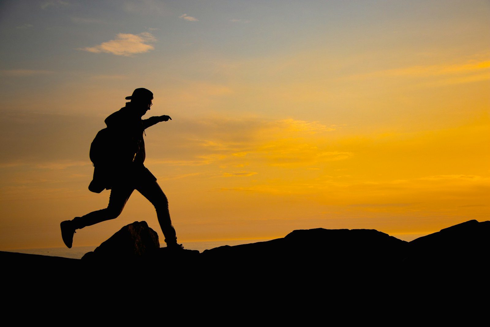 A silhouette of a person running on a hill at sunset